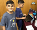 Two students, one is smiling at the camera, the other is using the chromebook to access a computer science program.