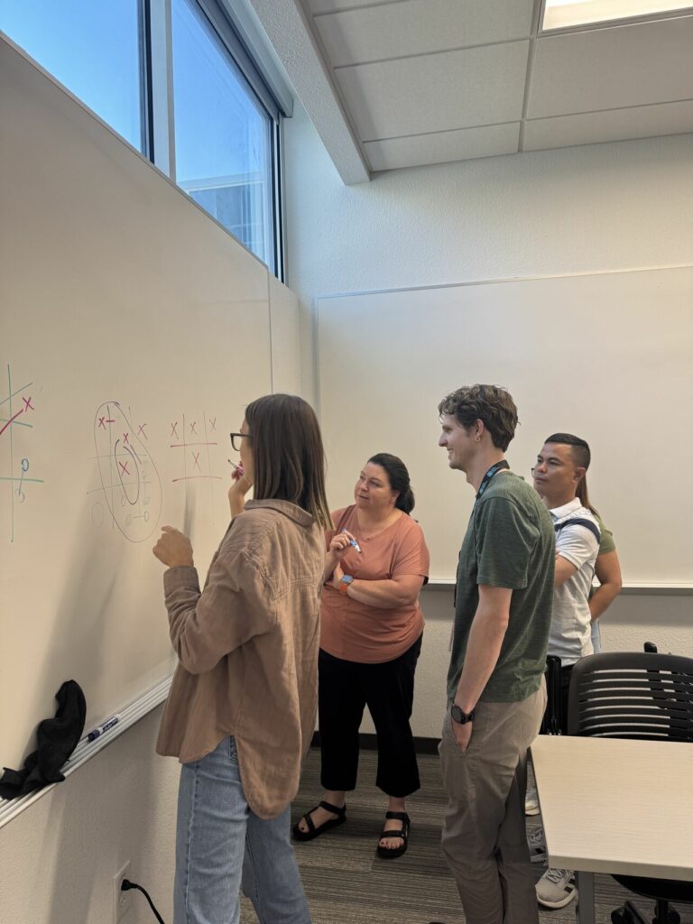 Four teachers playing tiq taq toe at the dry erase board. 